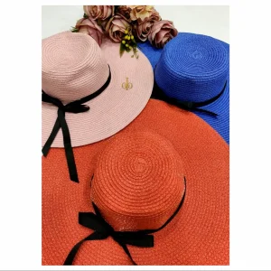 Three wide‑brim woven sun hats in pink, blue, and orange with black ribbon bows and floral accents.
