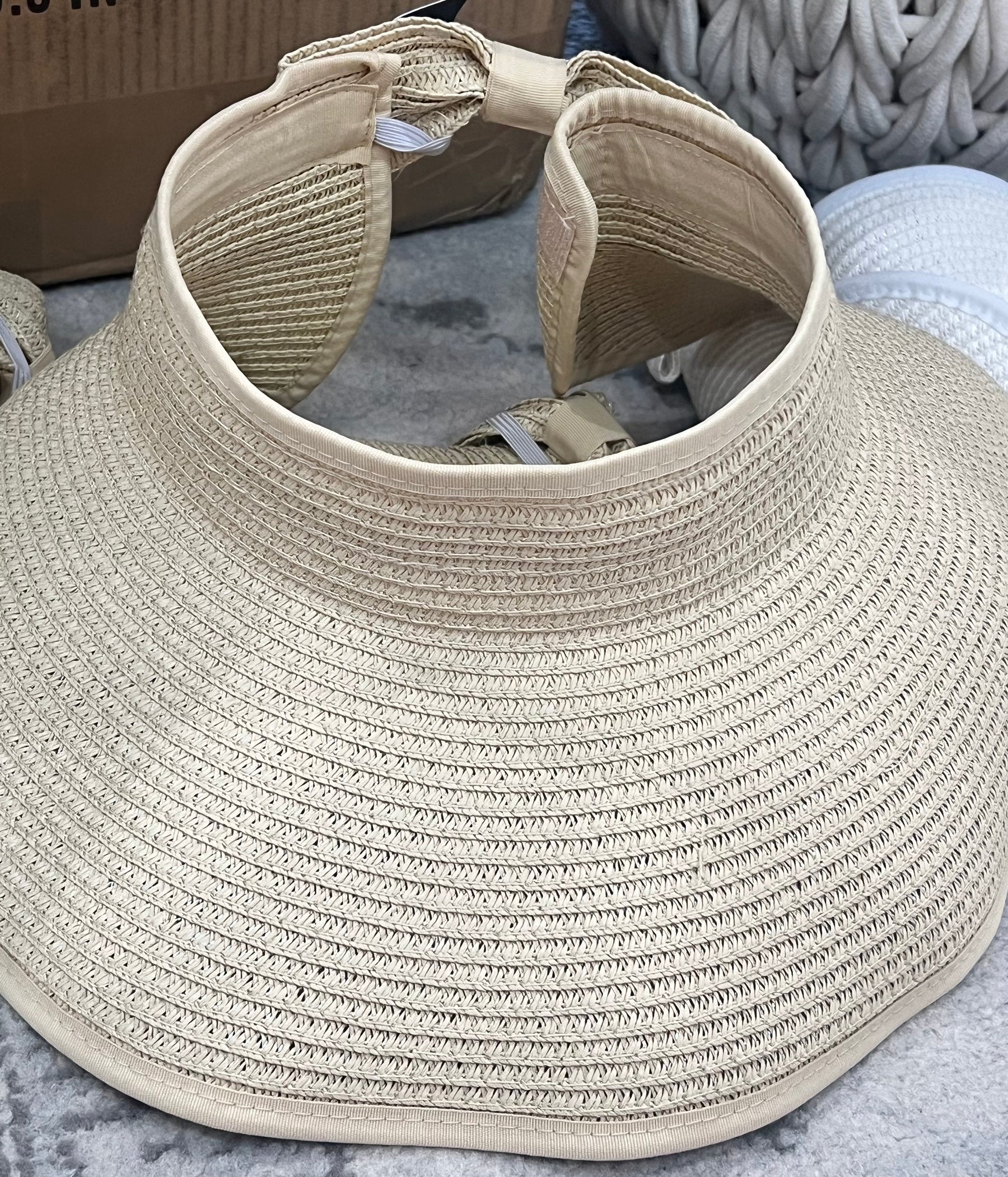 Beige woven straw sun visor hat with wide brim and adjustable strap.