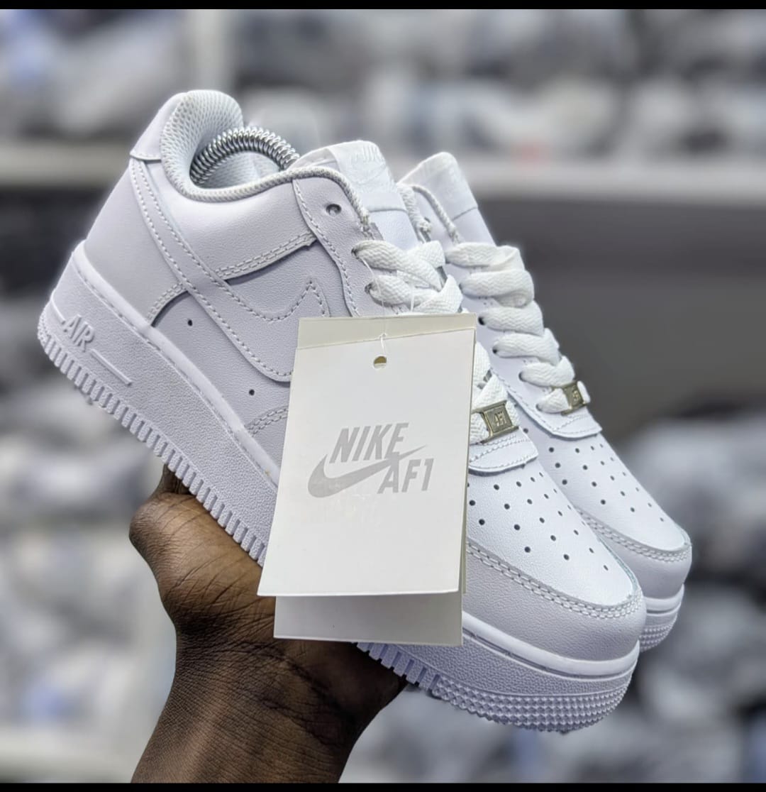 All‑white Nike Air Force 1 sneakers with leather upper, perforated toe box, white laces, and thick rubber sole embossed with 'AIR