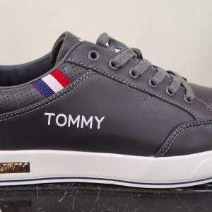 Black sneaker with white sole, black laces, and 'TOMMY' branding on side and metallic plate near heel, with red‑white‑blue fabric accent.